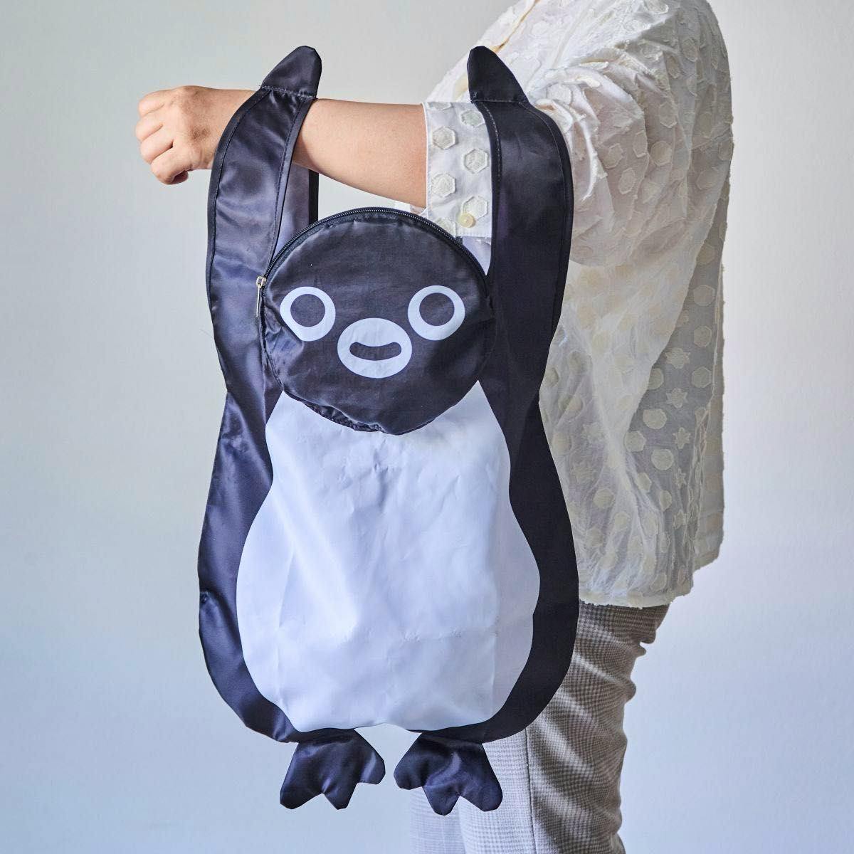 A Suica penguin-shaped hanging storage eco bag (polyurethane) held from a person’s arm, showing the front design.