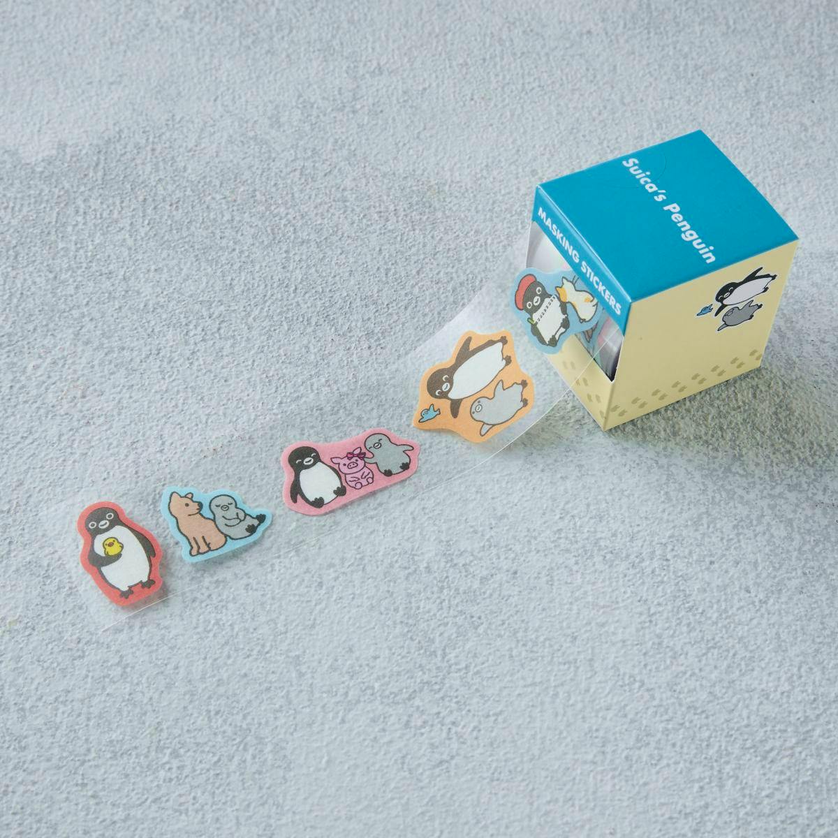 A small box of Suica's Penguin masking stickers with a clear strip of penguin-and-animal shaped stickers pulled out and several stickers displayed on the surface.
