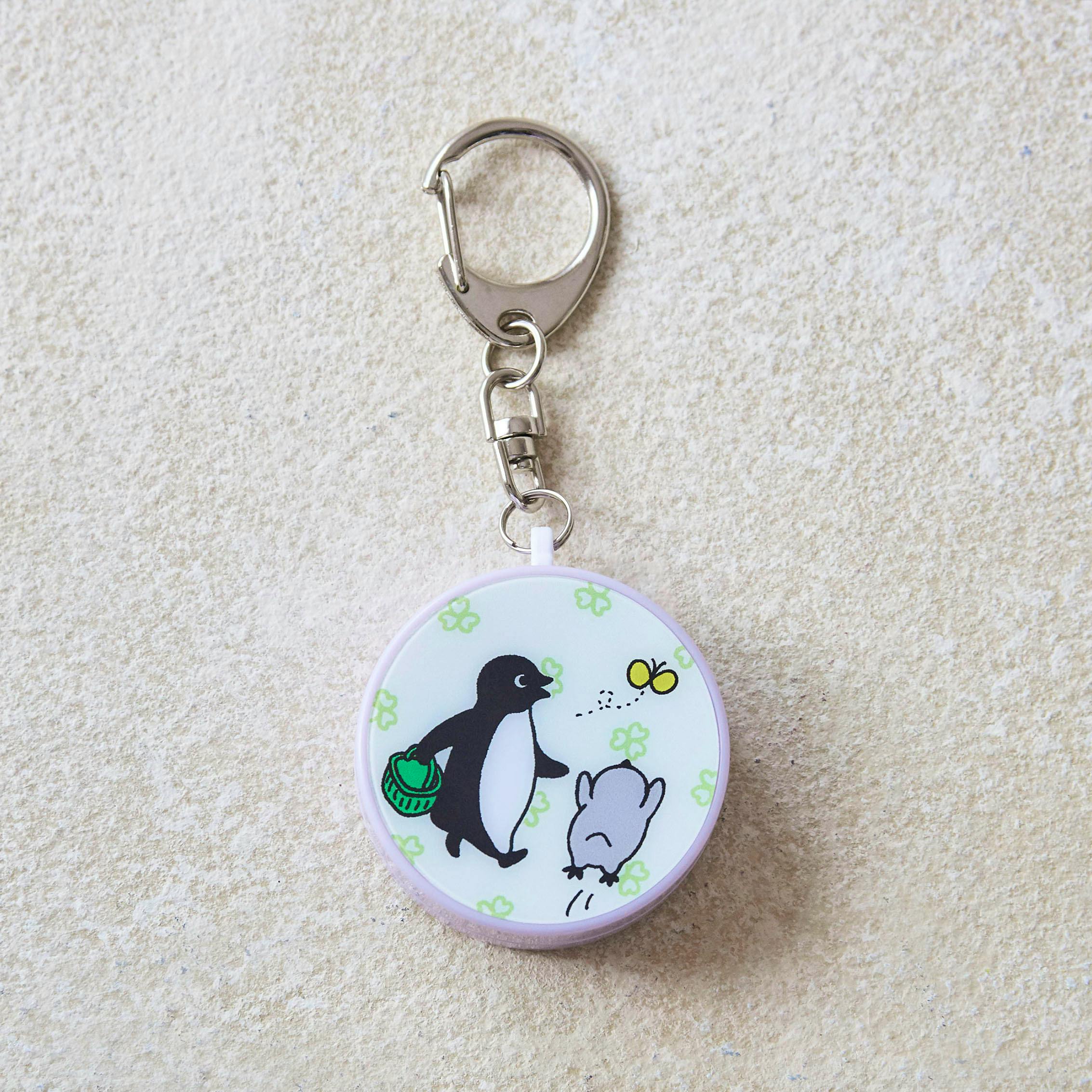 Round plastic keychain alarm with a Suica penguin illustration visible and a metal clasp above on a textured background.