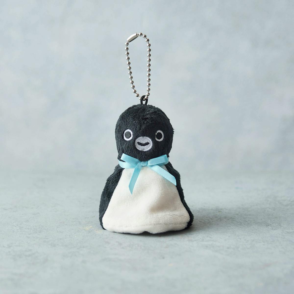Front view of the Suica penguin teruteru plush keychain showing its smiling face, white belly, blue ribbon, and metal ball chain.