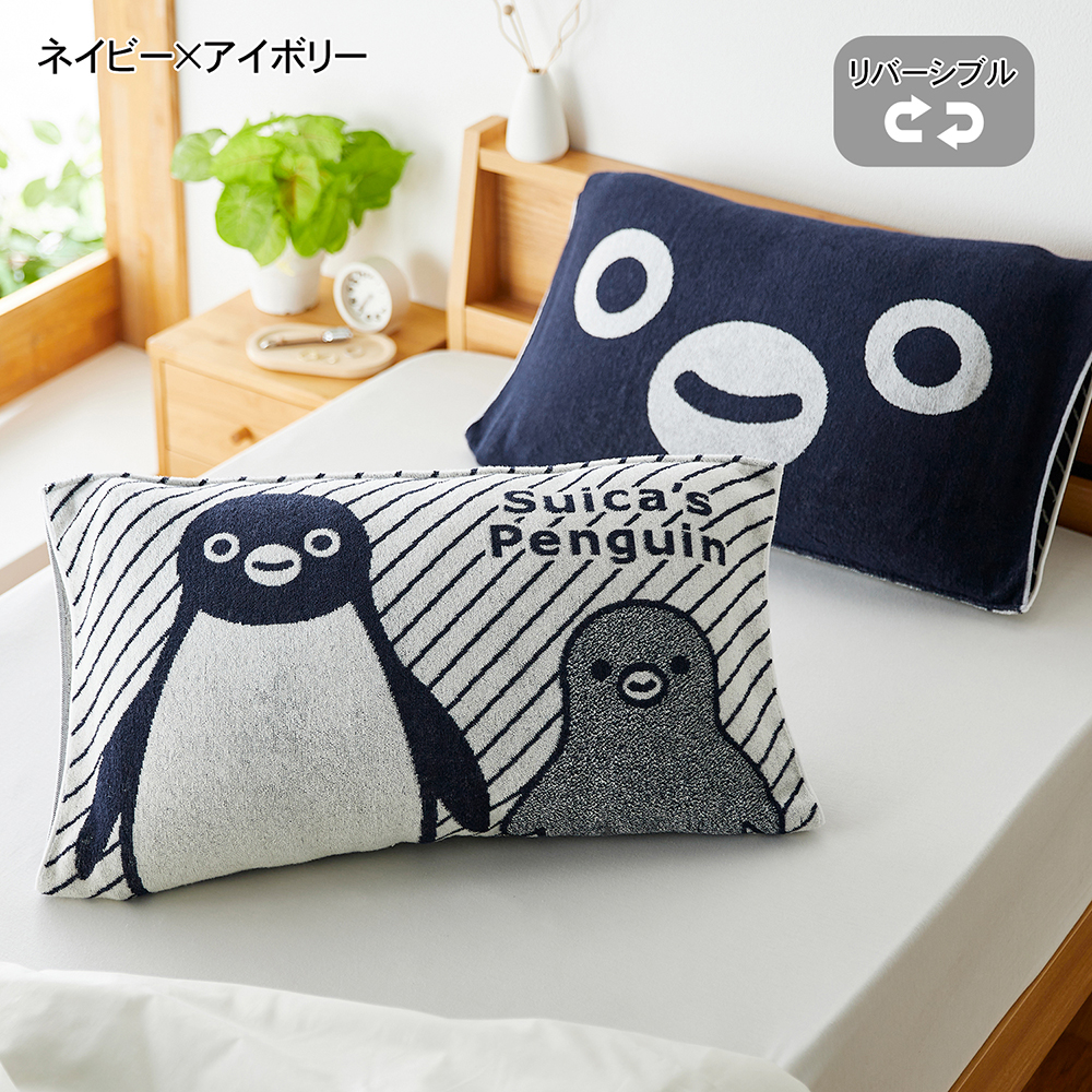 Two navy and ivory Suica Penguin pillow covers on a bed, showing the penguin-front design in the foreground and the navy reverse with face motif behind.