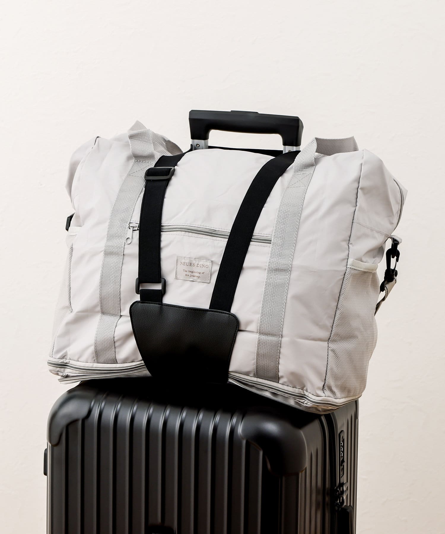A synthetic-leather carry-case band securing a light-colored duffel bag to the handle of a black hard-shell suitcase.