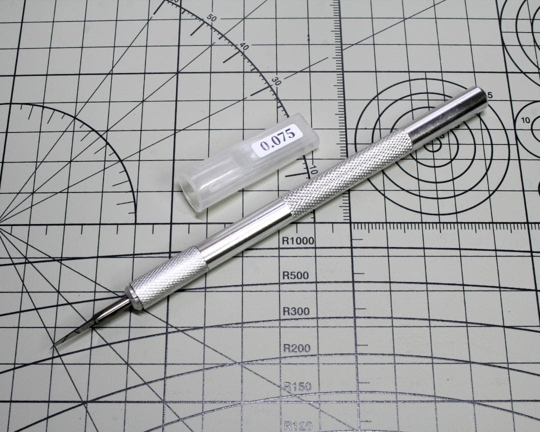 Silver metal chisel with knurled handle and small plastic cap labeled “0.075” on a cutting mat.