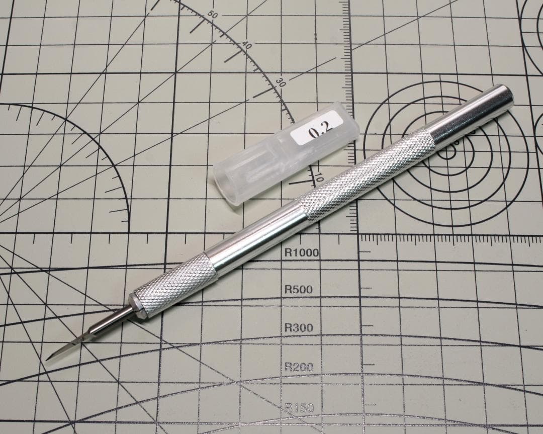 Silver chisel (0.2 mm) with a knurled handle and its plastic cap laid on a cutting mat.