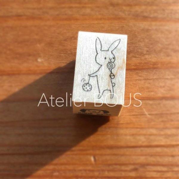 Wooden stamp block on a wooden surface showing a line-drawn rabbit holding two festival items on its top face.