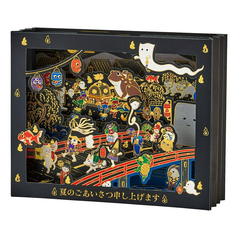 A black greeting card showing a colorful, gold-lined illustration of yokai and festival motifs with a die-cut window and Japanese text along the bottom.