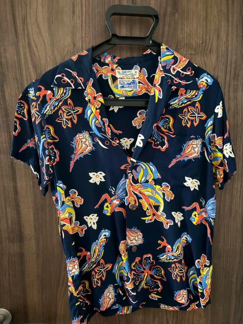 Navy SUN SURF × BEAMS short-sleeve aloha rayon shirt with multicolor tropical print hanging on a hanger against a wood background.