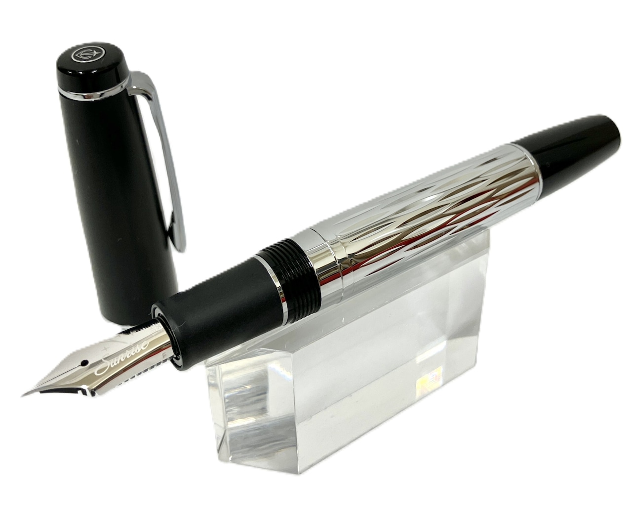 Silver-patterned fountain pen with black cap removed, resting on a clear display stand against a white background.