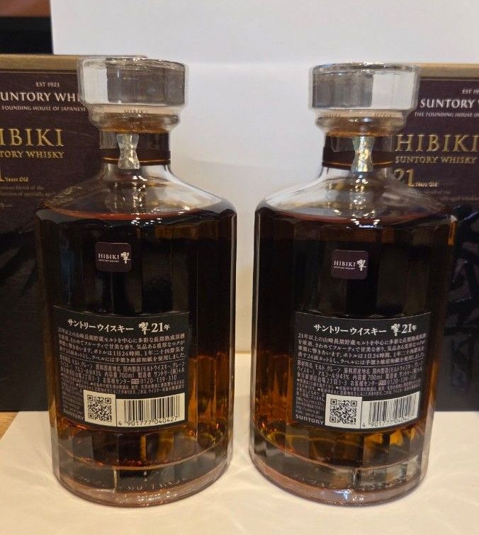Two Hibiki 21-year whisky bottles shown from the back with their boxes visible behind them.
