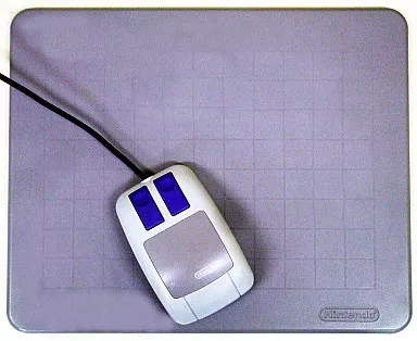 A Super Famicom mouse with its cable resting on a gray grid-pattern mouse pad.