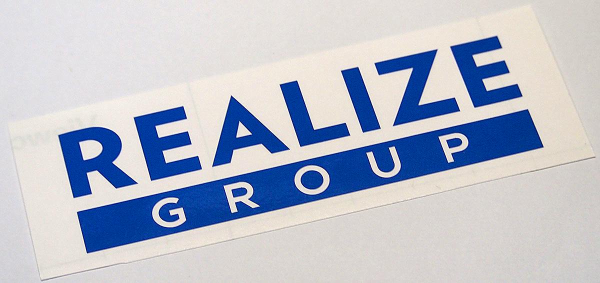 Blue "REALIZE GROUP" paper sticker on a white backing sheet.
