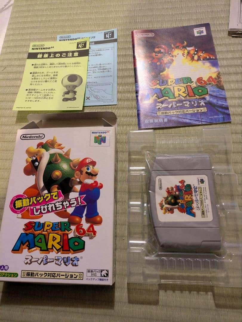 Super Mario 64 (Nintendo 64) game box, instruction booklet, and grey cartridge in a plastic tray on a tatami mat.