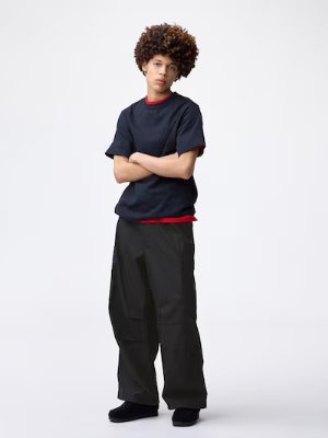 Male model wearing the black super wide cargo pants, standing with arms crossed.