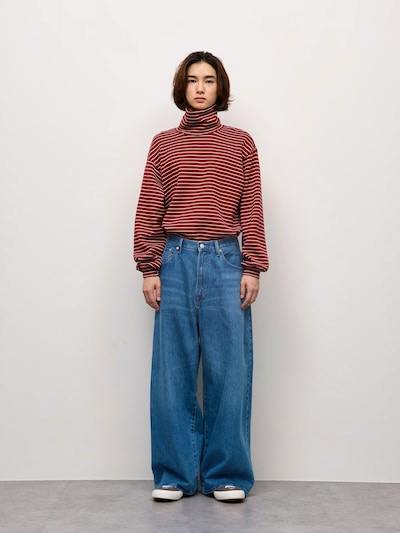 A model standing against a plain wall wearing light-blue wide men's jeans.