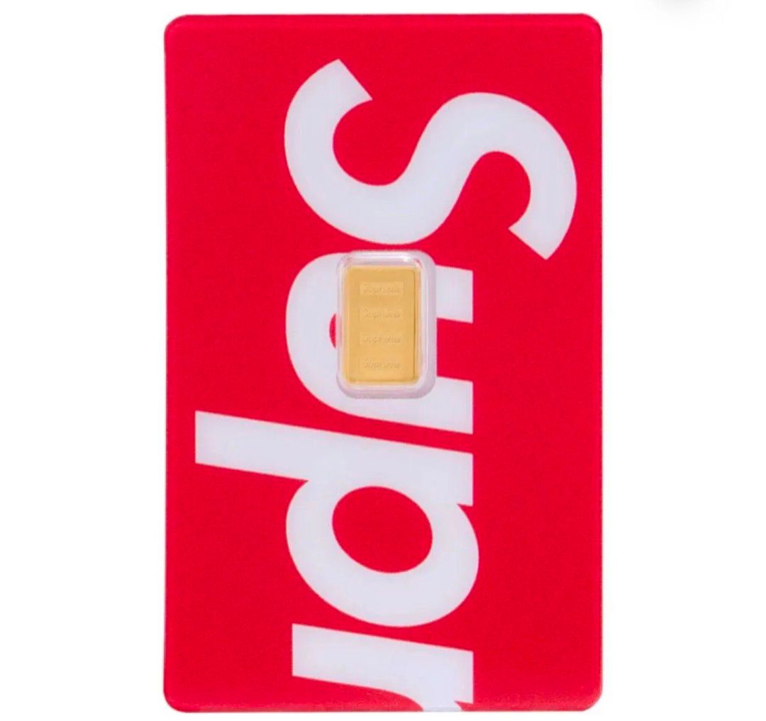 A 1 g PAMP Suisse gold bar displayed in its blister pack on a red Supreme card.