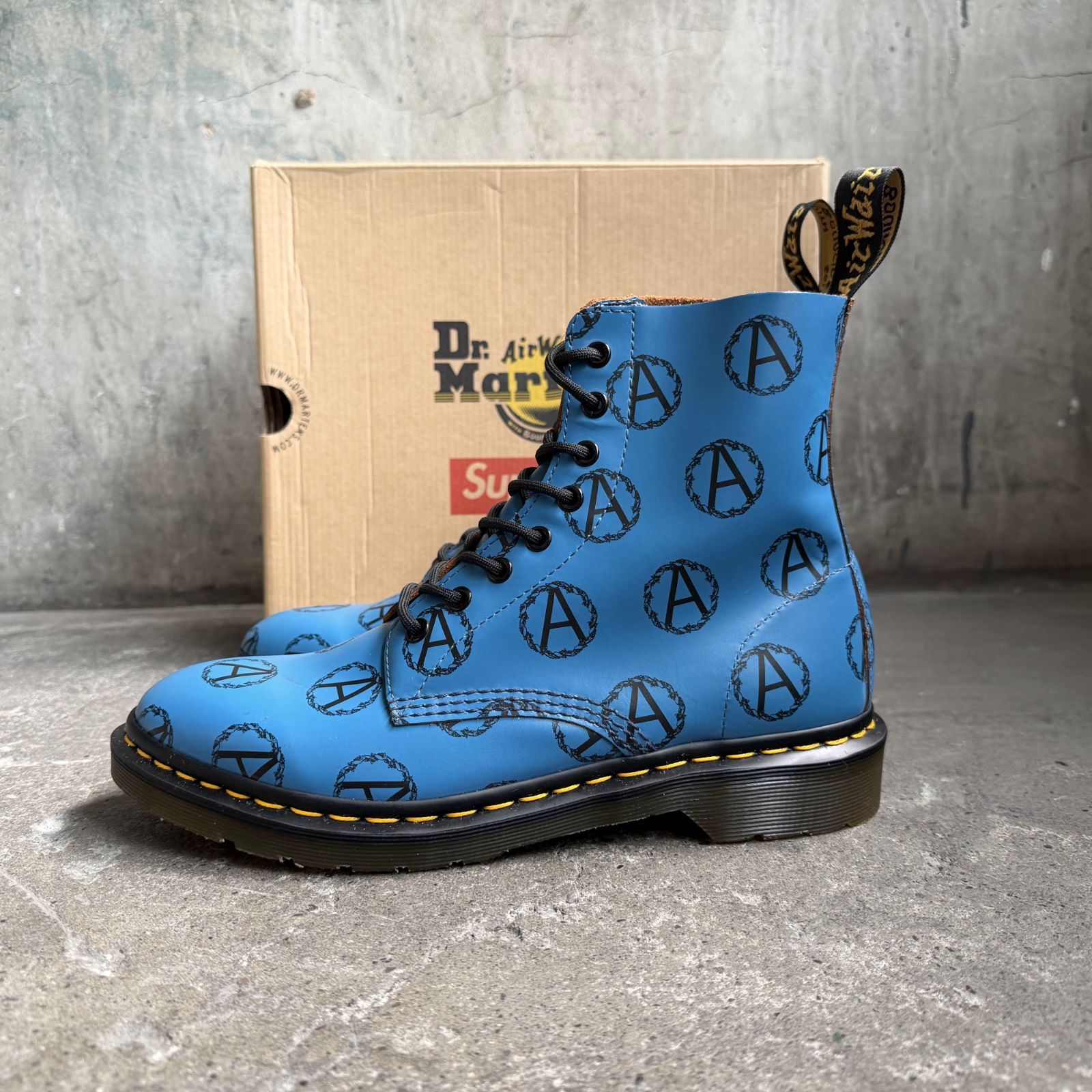 Blue 8-eye boot with black anarchy 'A' print and Dr. Martens box behind it.
