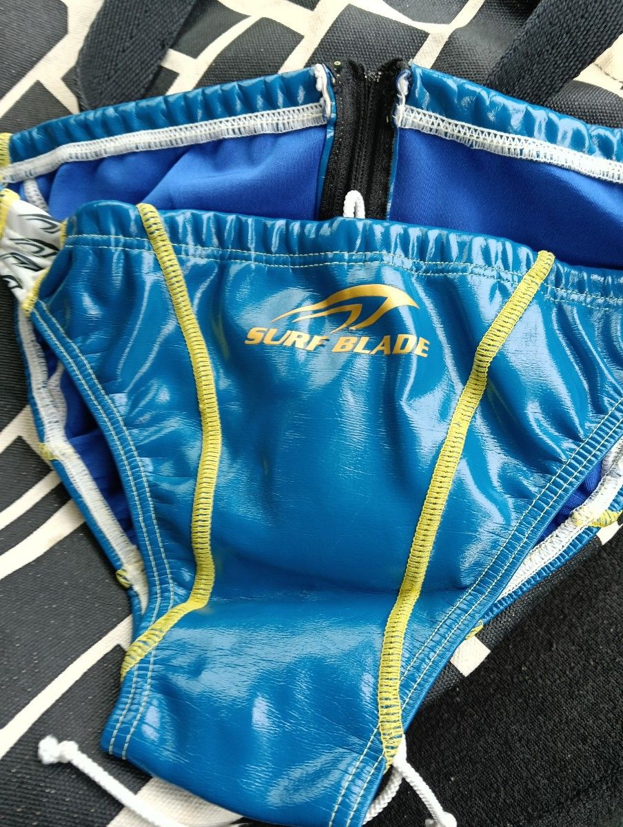 Blue SURF BLADE men's racing swimsuit (competitive briefs) front view laid flat showing logo and yellow trim.