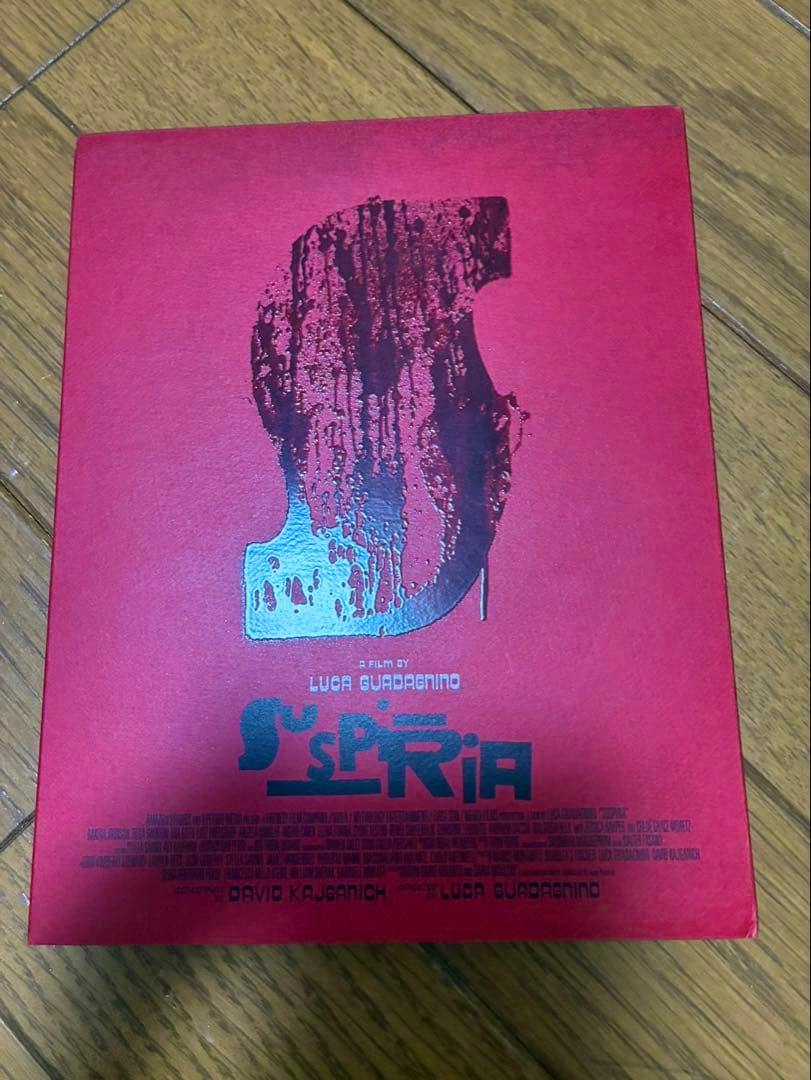 Red Suspiria Blu-ray first‑press outer box with a stylized 'S' artwork photographed on a wooden floor.