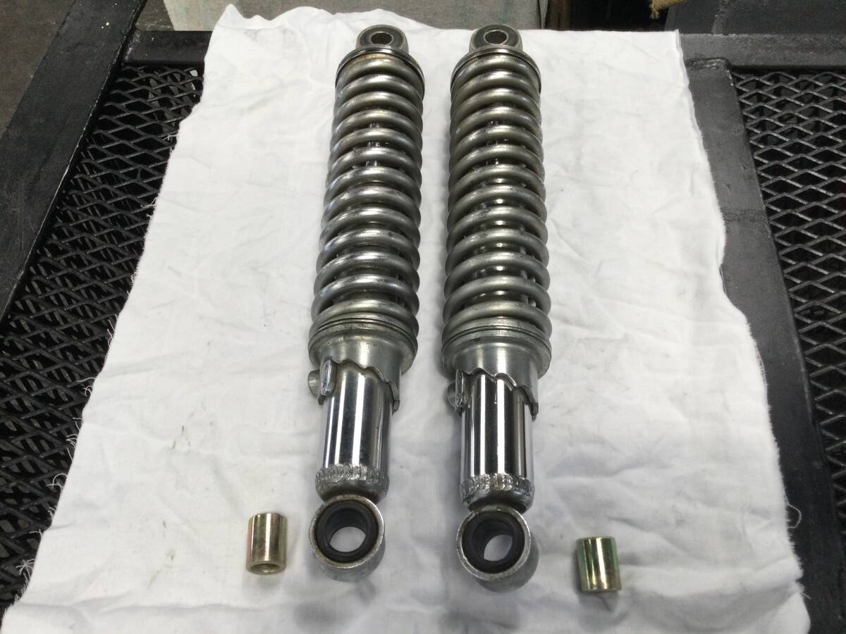 A pair of metal suspension shock absorbers for a Suzuki GT250 laid on a white cloth with two small metal bushings.