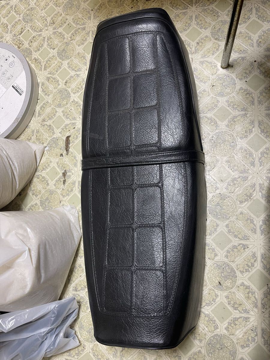 Top view of a black motorcycle seat for a Suzuki RG250 showing the patterned cover and central strap.