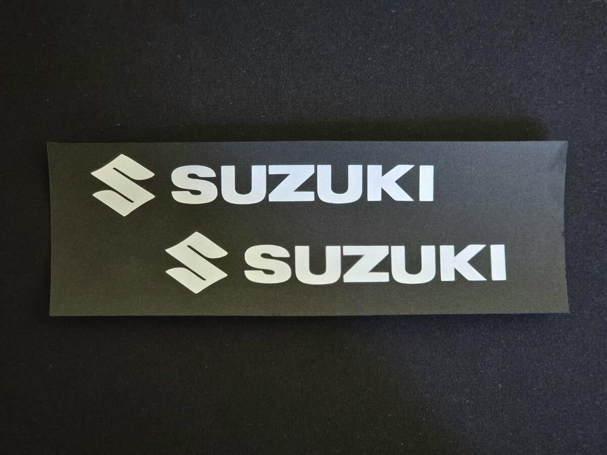 Two white SUZUKI word stickers and two white Suzuki emblem stickers displayed on a black backing sheet.