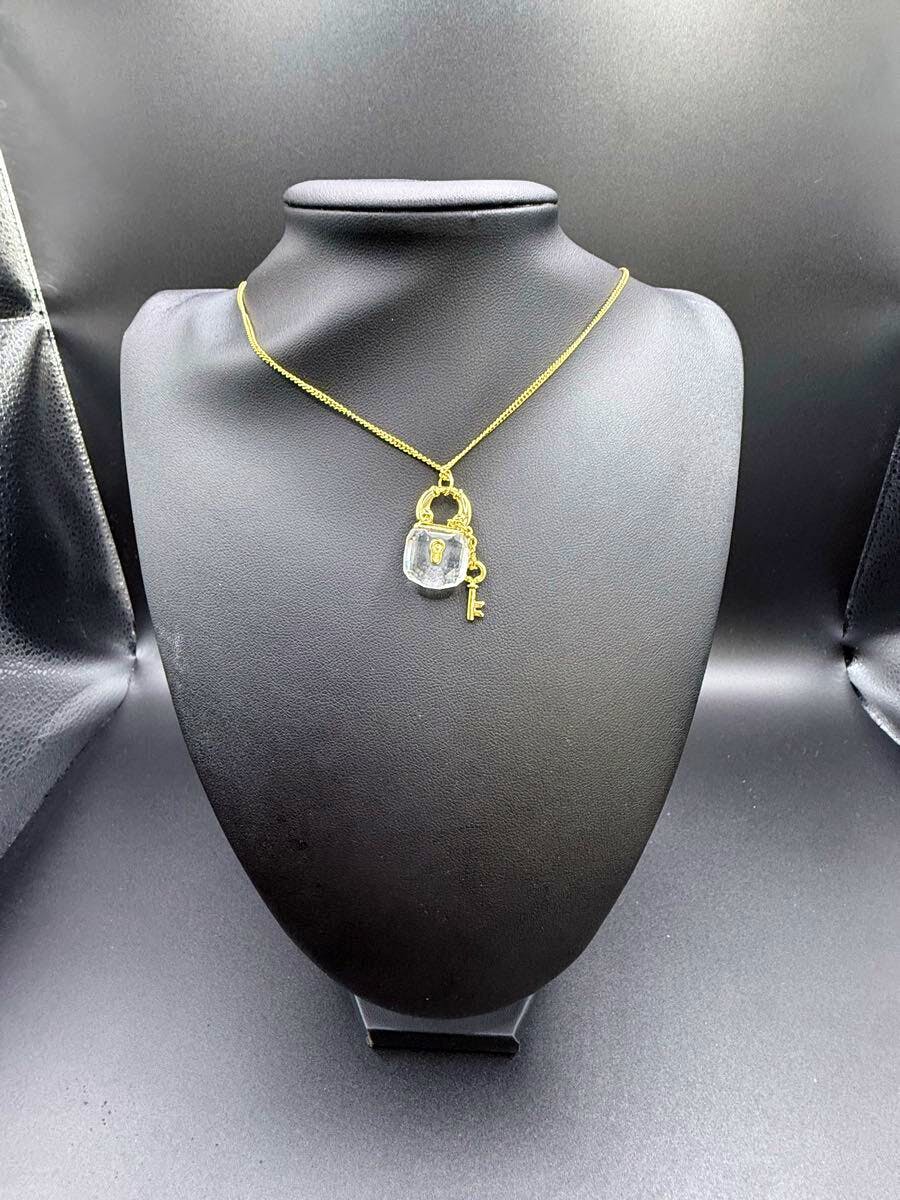 Gold-colored necklace with a clear-stone padlock pendant and a small key displayed on a black necklace bust.