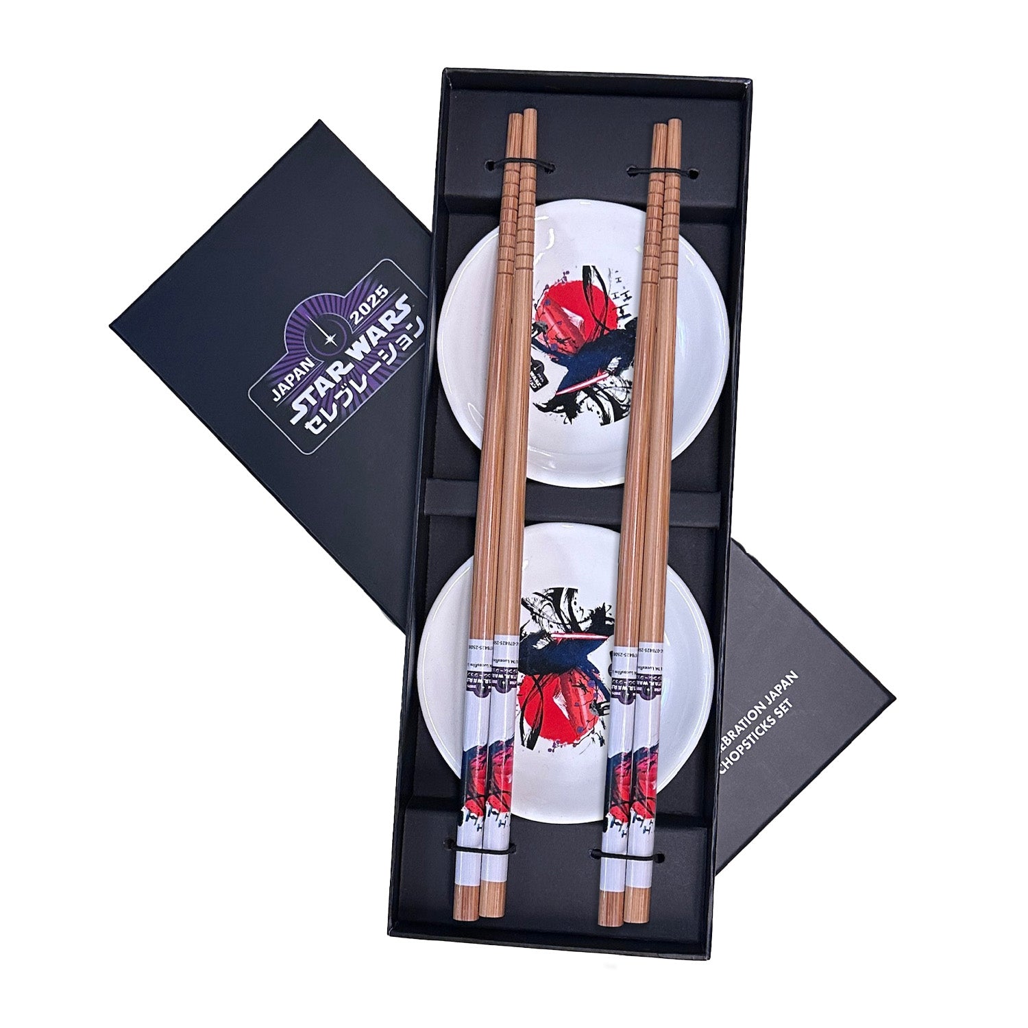 Two pairs of wooden chopsticks with decorative printed handles and two small soy sauce dishes arranged in a black presentation box.