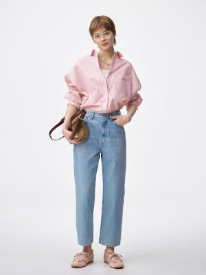 Woman modeling light blue ankle-length women's jeans while wearing a pink shirt and carrying a small bag.