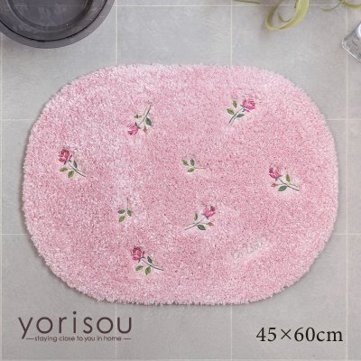 Pink oval 45×60cm bath mat with scattered small rose motifs displayed on a tiled floor.