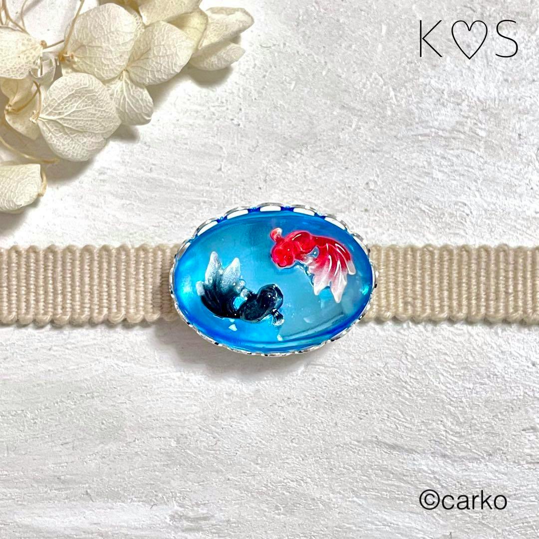Oval blue glass obi-dome with a red and a black goldfish shown on a beige obi band.