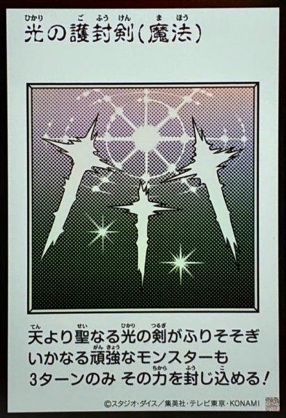 Photograph of the trading card front showing monochrome artwork of three glowing sword-like shapes with a circular light pattern, the Japanese title, and descriptive Japanese text.