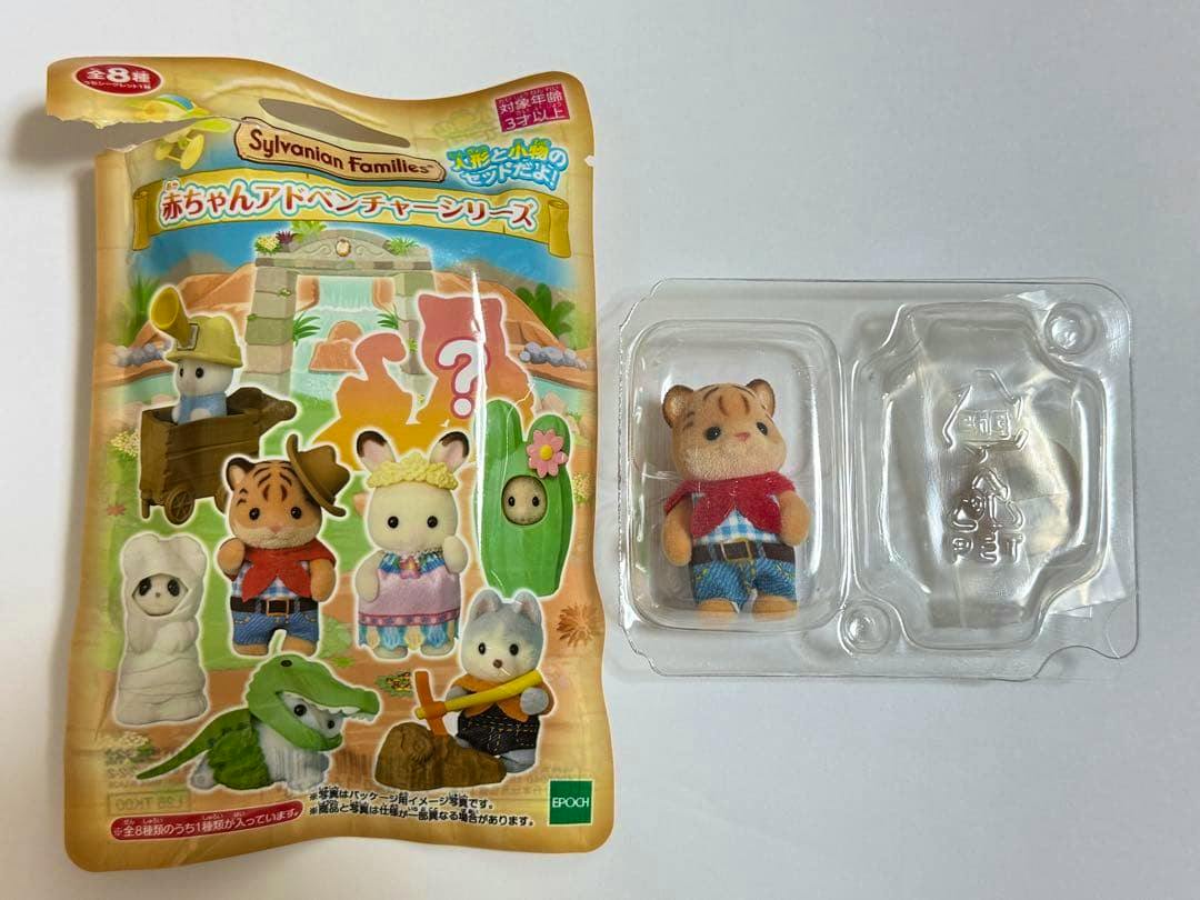 Sylvanian Families tiger baby figure in a clear plastic blister tray next to its illustrated Baby Adventure Series packaging.