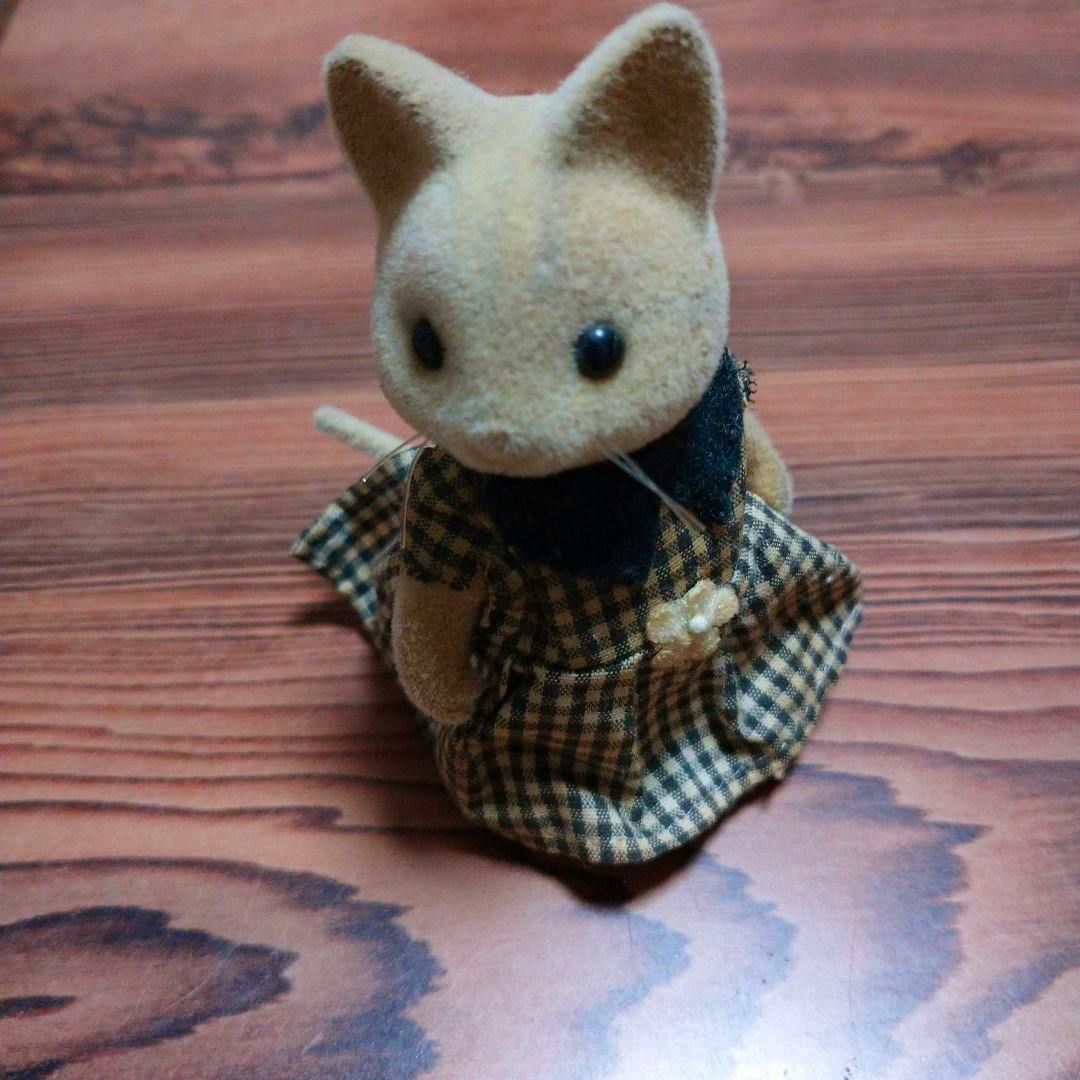A Sylvanian Families cat doll in a checkered dress posed on a wood-grain surface.