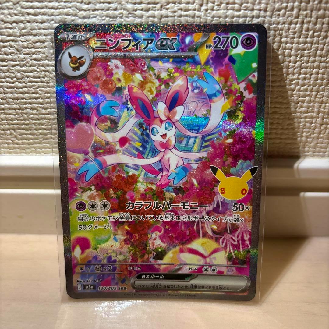 Front holographic image of the ニンフィアex trading card (Pokémon) showing the character artwork, Japanese text, HP, and attack details in a protective sleeve.
