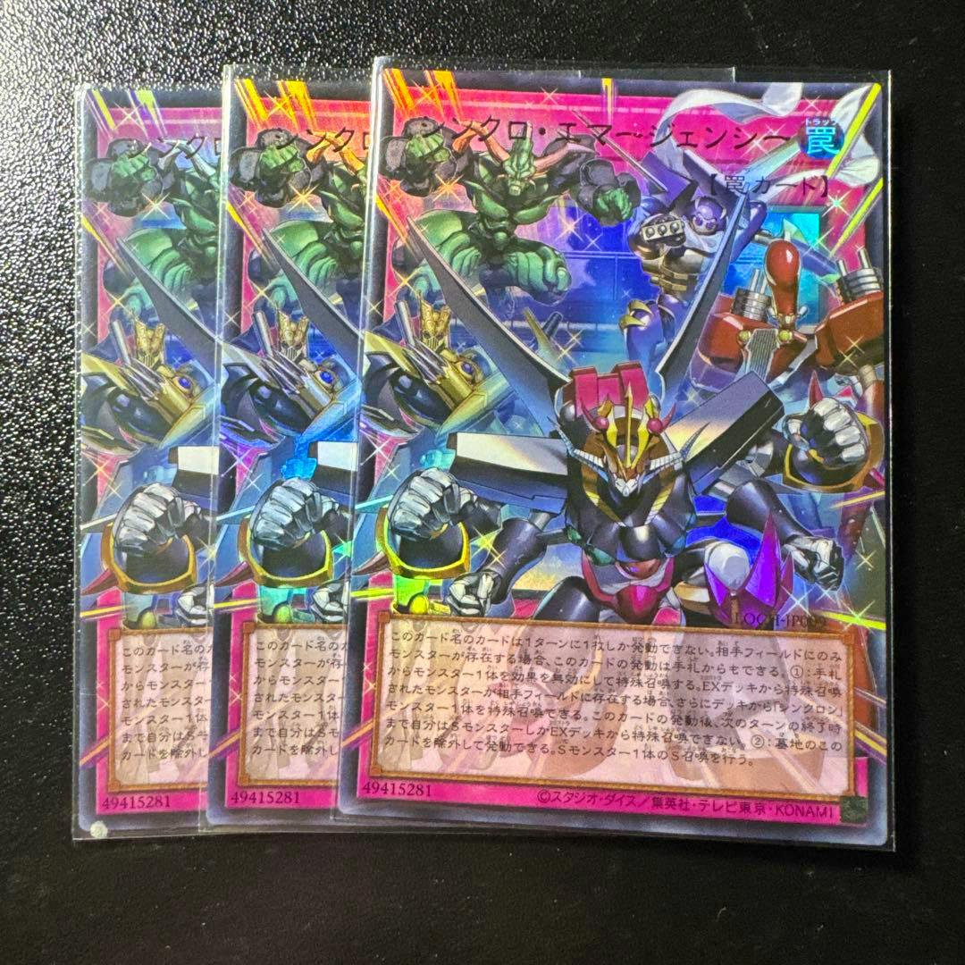 Three Asian-version trading cards of シンクロ・エマージェンシー　オーバーフレーム　ウルトラ in protective sleeves shown overlapping on a black surface.