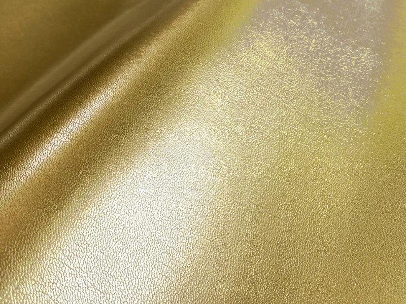 Close-up of thin gold synthetic leather (polyester) fabric showing a shiny textured surface and slight drape.
