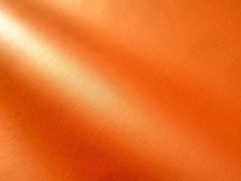 Close-up of thin orange matte synthetic leather (polyester) fabric showing texture and a gentle fold.