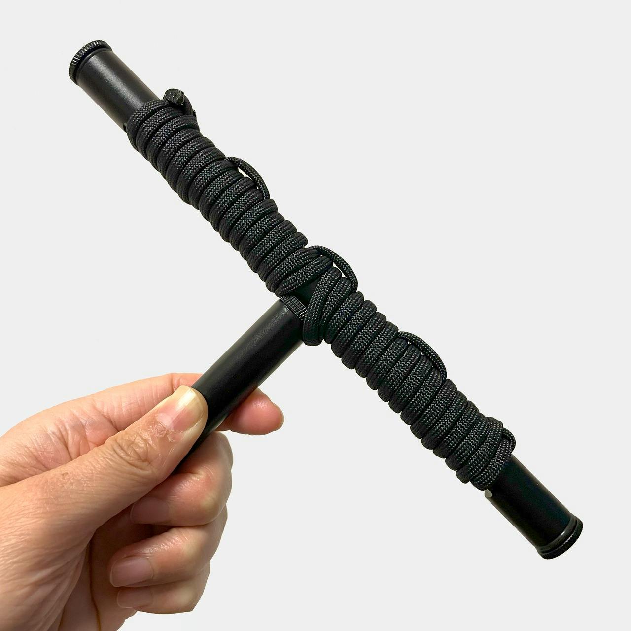 A hand holds a black T-shaped plastic perch for small owls wrapped in black cord.