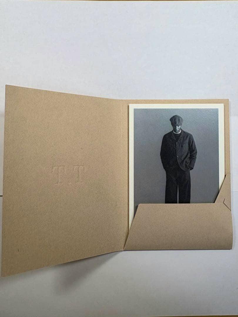 Open kraft folder of the T.T postcard set with a postcard showing a monochrome photo of a standing person in dark clothing.