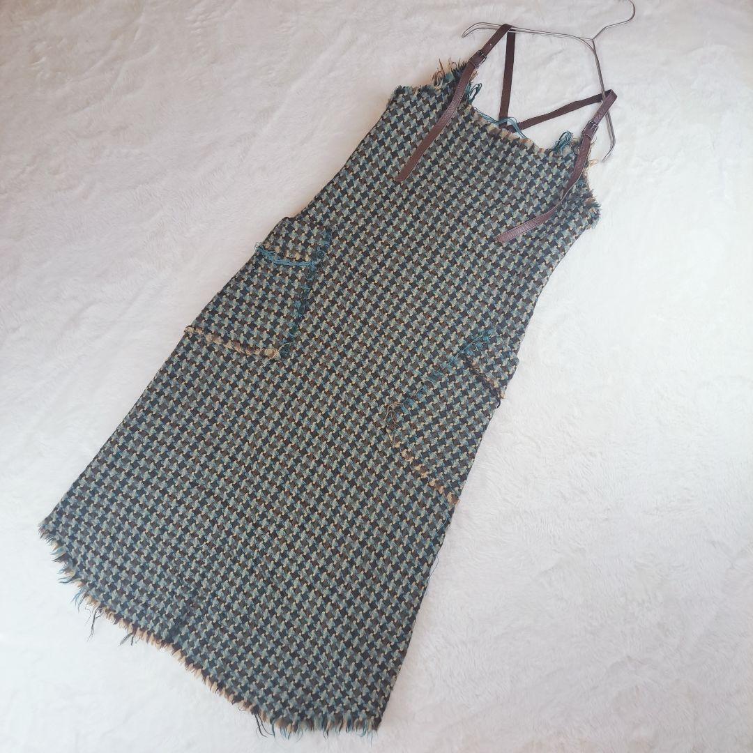 A wool jumper dress with leather shoulder straps laid flat on a white background.
