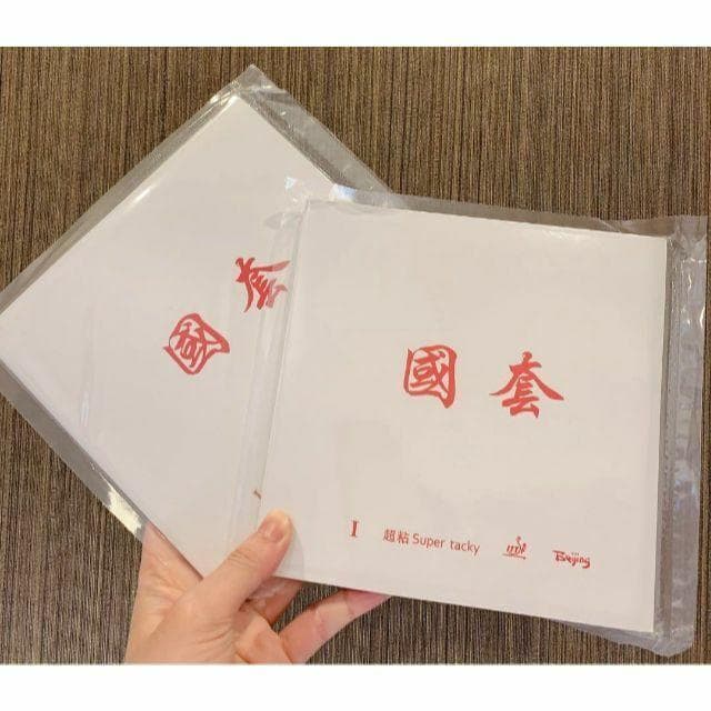 A hand holding two packaged table tennis racket rubbers with white covers and red Chinese characters.