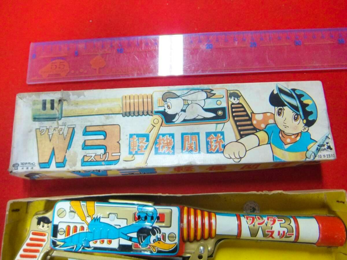 Top view of the boxed W3 (Wonder Three) toy light machine gun showing the illustrated box art and part of the zinc-alloy toy inside next to a ruler.