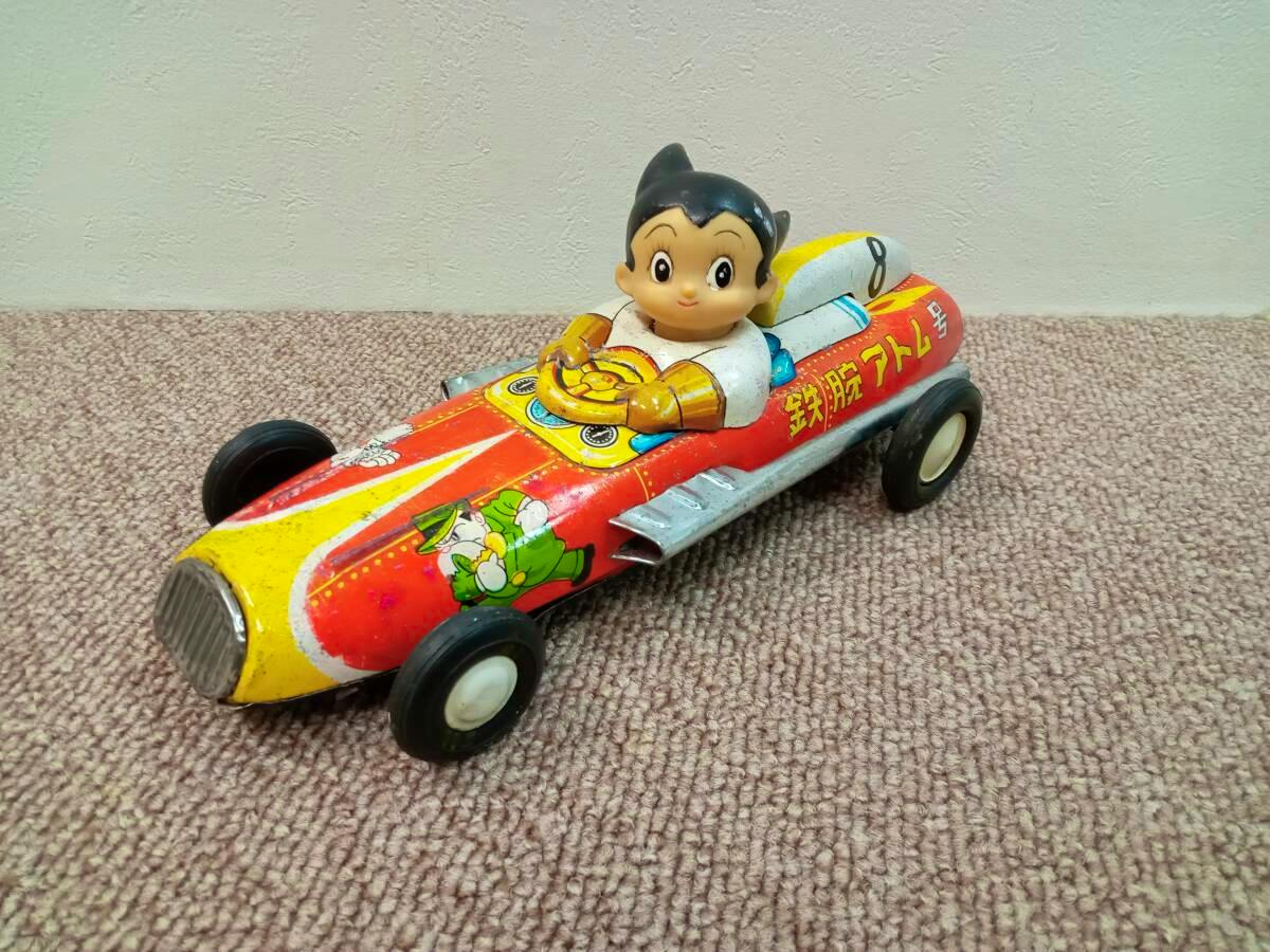 Tin Tetsuwan Atom (Astro Boy) race car toy showing the Atom figure seated in a red and yellow metal racing car.