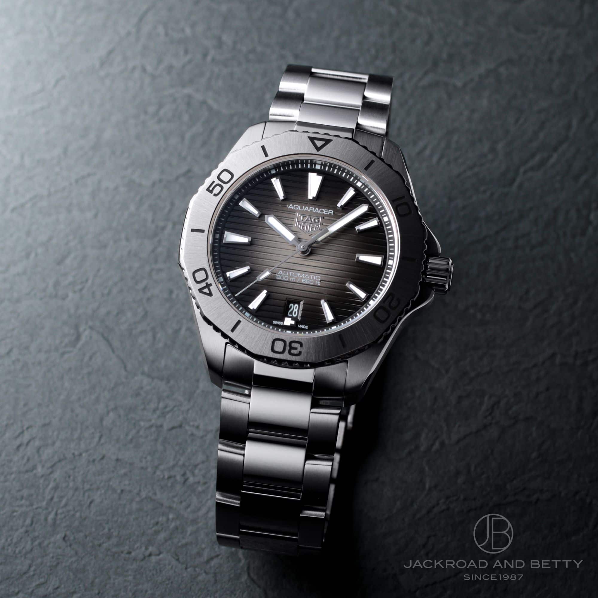 A TAG HEUER Aquaracer Professional 200 stainless steel wristwatch with a dark striped dial and metal bracelet photographed at an angle on a dark textured surface.