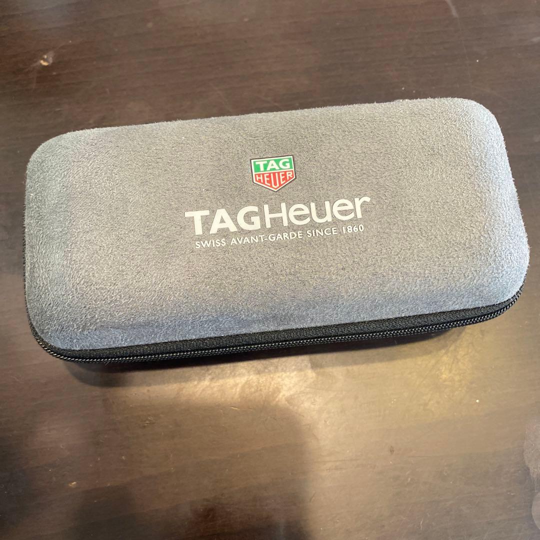 Gray TAG Heuer zippered watch case with the TAG Heuer logo on top, shown on a wooden surface.
