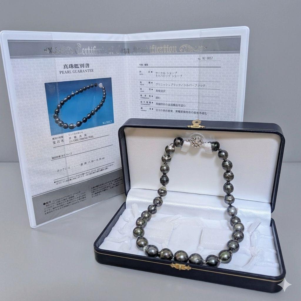Tahitian black pearl necklace with round semi-baroque pearls displayed in an open box alongside its certificate.