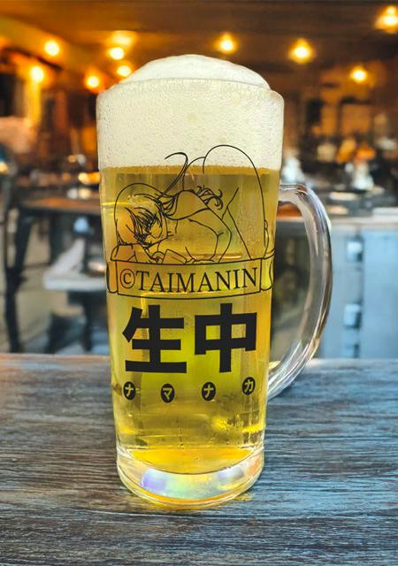 Glass beer mug filled with beer and foam, printed with an anime character, "TAIMANIN" and Japanese text.