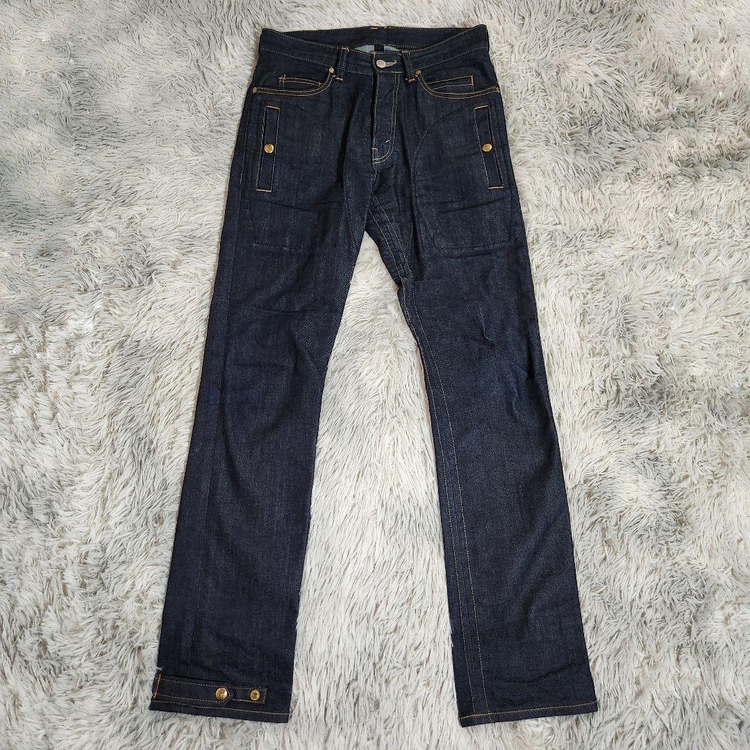 Flat-lay photo of indigo denim men's jeans (TAKAHIROMIYASHITATheSoloist.) laid on a light textured surface.