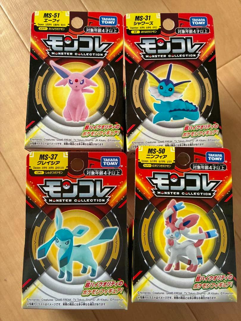 Front view photo of four Takara Tomy Monster Collection Pokémon figure boxes (Espeon, Vaporeon, Glaceon, Sylveon) arranged in a two-by-two grid on a wooden surface.