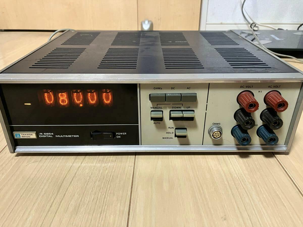Front view of the Takeda Riken digital multimeter showing illuminated nixie tube digits, control buttons, and multiple voltage/ohm banana-jack terminals.